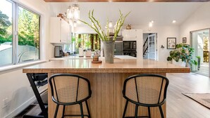 Een moderne keuken met een groot eiland, twee barkrukken en een potplant.