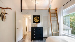 Een slaapkamer met een bed, een kapstok, een ladder, een aan de muur hangend schilderij en een deur naar een andere kamer.