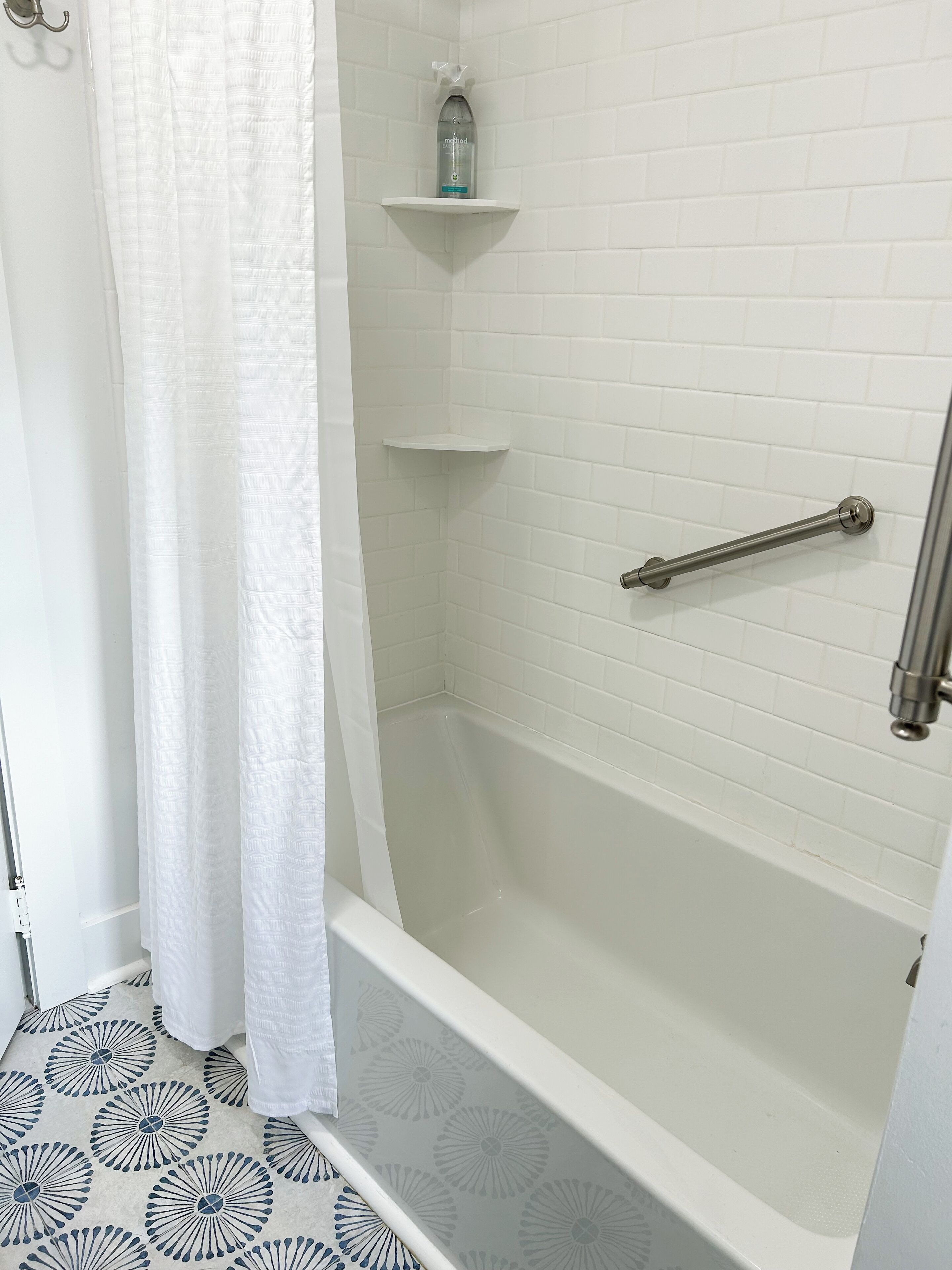 A bathroom with a bathtub, a shower, and a toilet. There are white tiles on the walls and floor, and a shower curtain.