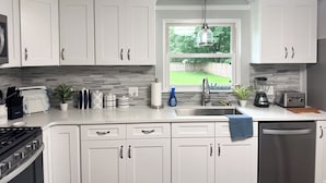 A modern kitchen with white cabinets, a stainless steel sink, and a window with a view of a backyard. - Delightful, newly renovated, 3 bedroom cape in a charming country setting  (Marilla)