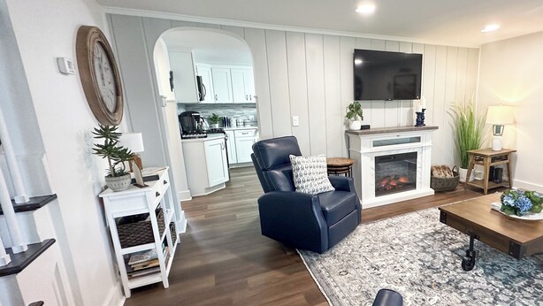 A living room with a fireplace, a television, and a kitchen in the background. - Delightful, newly renovated, 3 bedroom cape in a charming country setting  (Marilla)