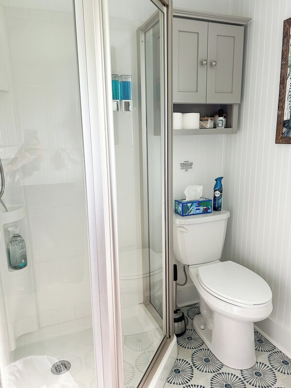 A bathroom with a glass shower enclosure, a toilet, and a cabinet above the toilet.