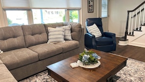 A living room with a grey sofa, a blue armchair, and a wooden coffee table with a vase of flowers. - Delightful, newly renovated, 3 bedroom cape in a charming country setting  (Marilla)