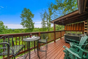 A wooden deck with outdoor seating, a hot tub, and a view of a forested area.