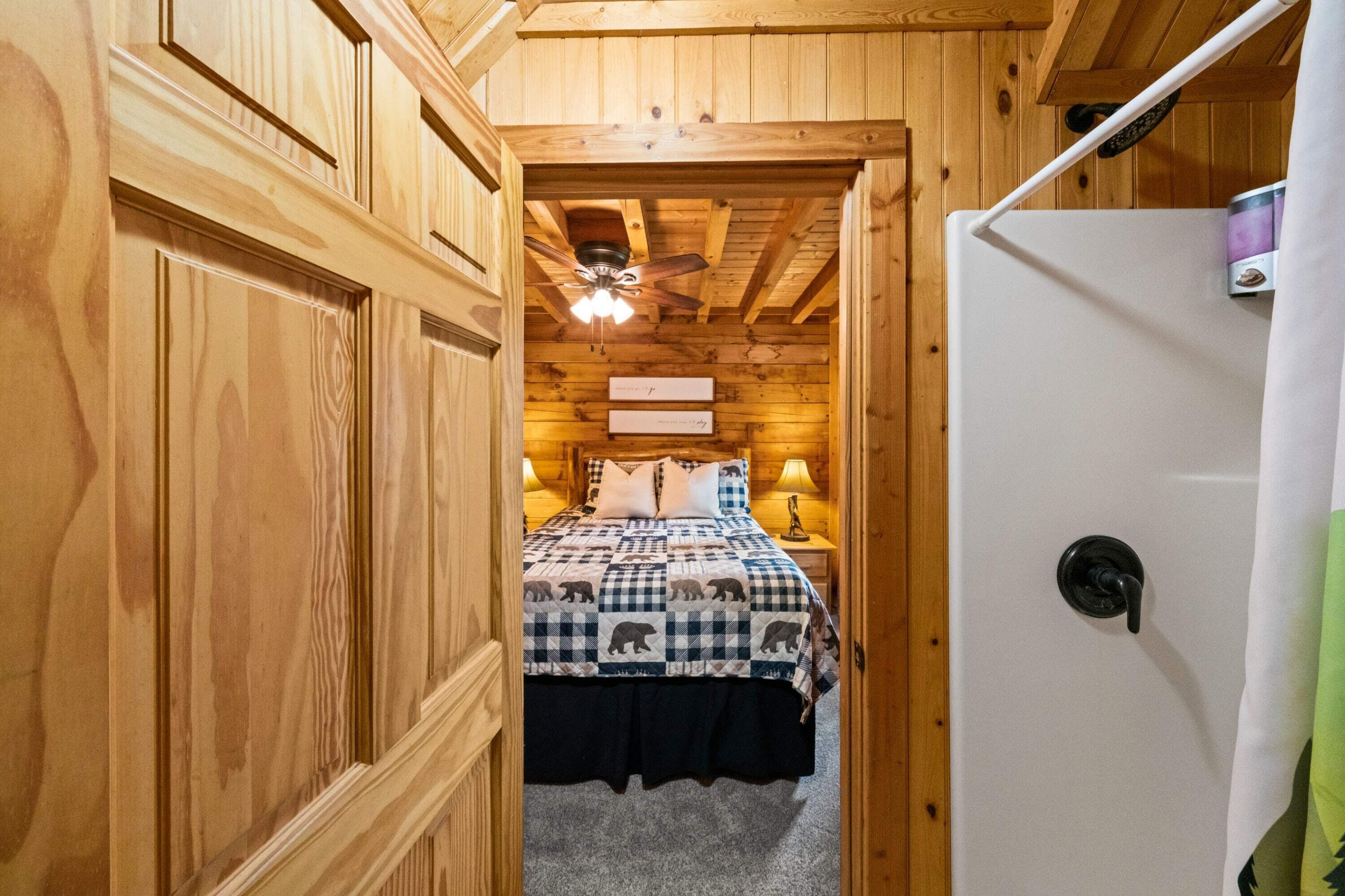A wooden cabin interior with a bed, a ceiling fan, and a white refrigerator.