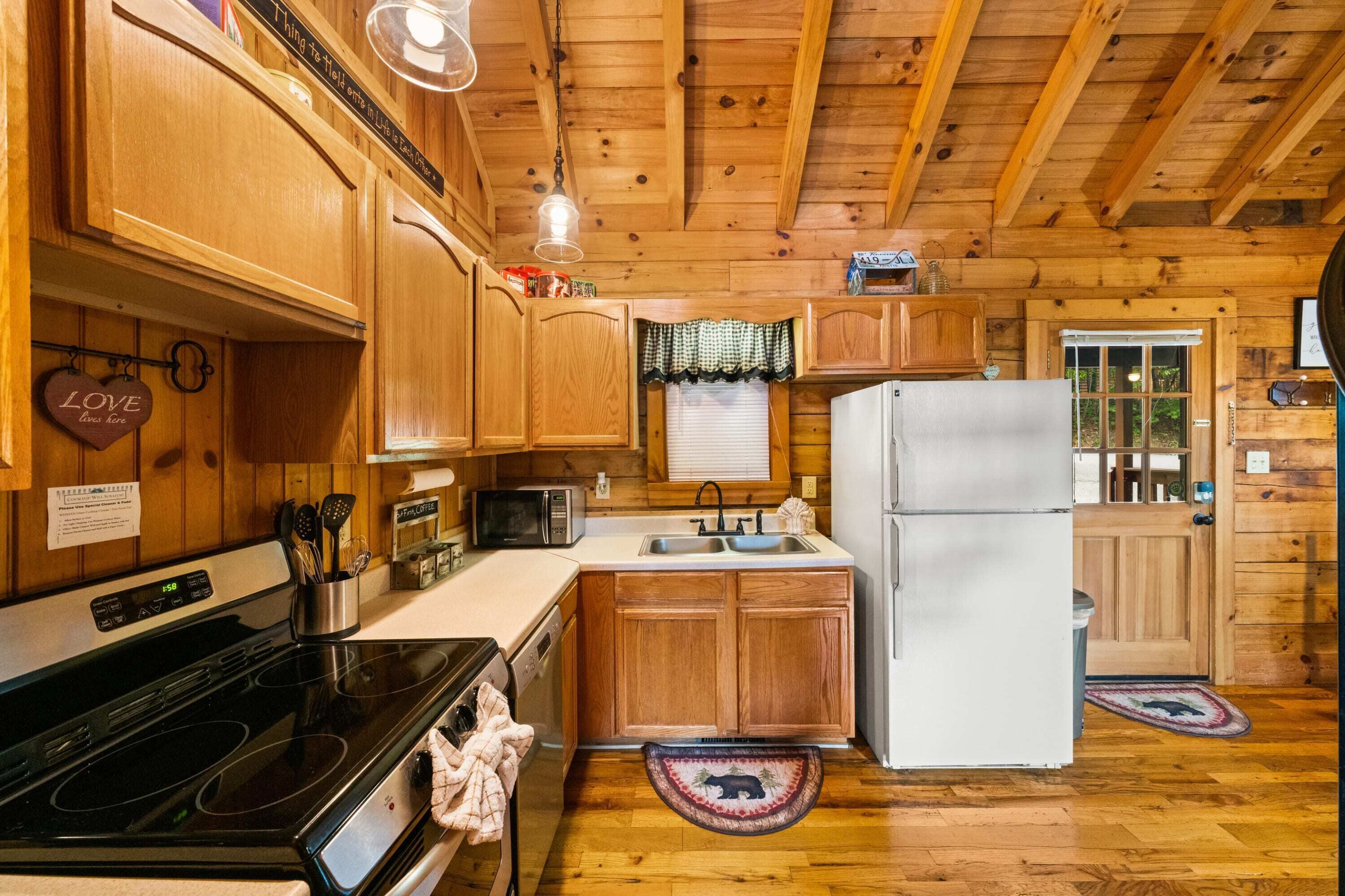 A wooden cabin kitchen with a stove, sink, refrigerator, and wooden cabinets.
