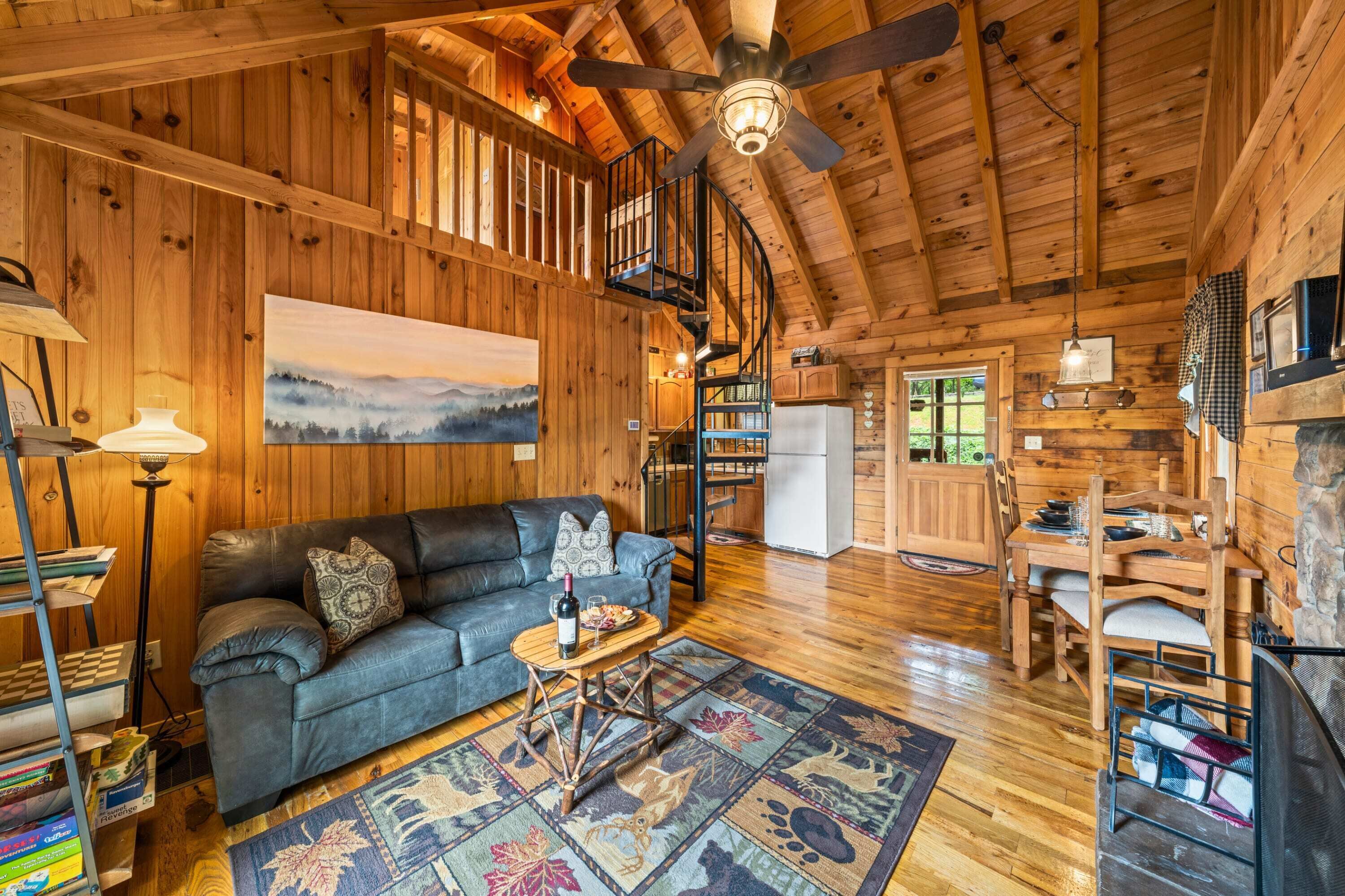 A wooden cabin interior with a sofa, dining table, and a ceiling fan.