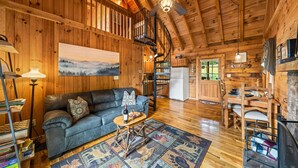 L’intérieur d’un chalet en bois, avec un canapé, une table à manger et un ventilateur de plafond.