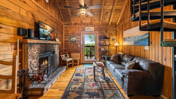 L’intérieur chaleureux d’un chalet avec une cheminée en pierre, un canapé en cuir, des murs en bois et un escalier.