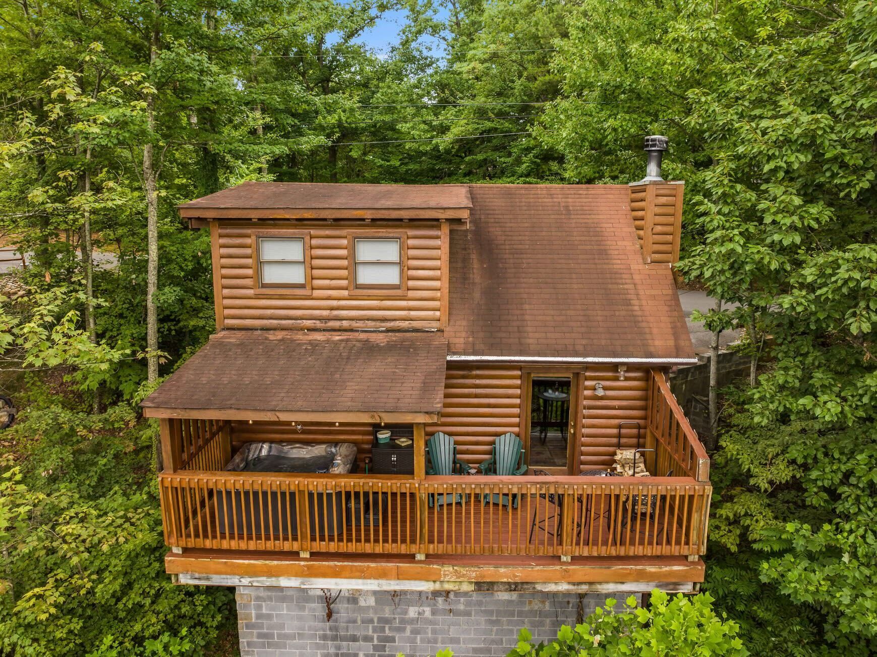 A two-story log cabin with a balcony, surrounded by dense forest.