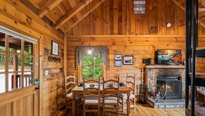 L’intérieur d’un chalet en bois, avec une table à manger, des chaises, une cheminée et une vue sur l’extérieur par une fenêtre.