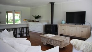 A modern living room with a white sofa, wooden coffee table, and a TV on a wooden cabinet. - Kurraba - Family friendly country escape with pool (Kangaroo Valley)
