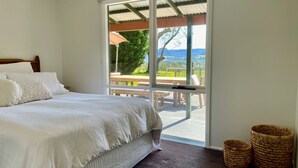 A bedroom with a large bed, a view of a patio with a table and chairs, and two woven baskets on the floor. - Kurraba - Family friendly country escape with pool (Kangaroo Valley)
