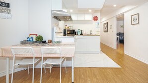 Cocina compacta con armarios blancos, microondas y estufa. Hay una mesa de comedor con dos sillas y una pequeña planta en maceta.