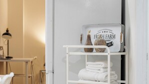 Un carro metálico blanco con toallas dobladas y un letrero que dice 'Fresh Farm', ubicado contra una pared blanca en una habitación con piso de madera.