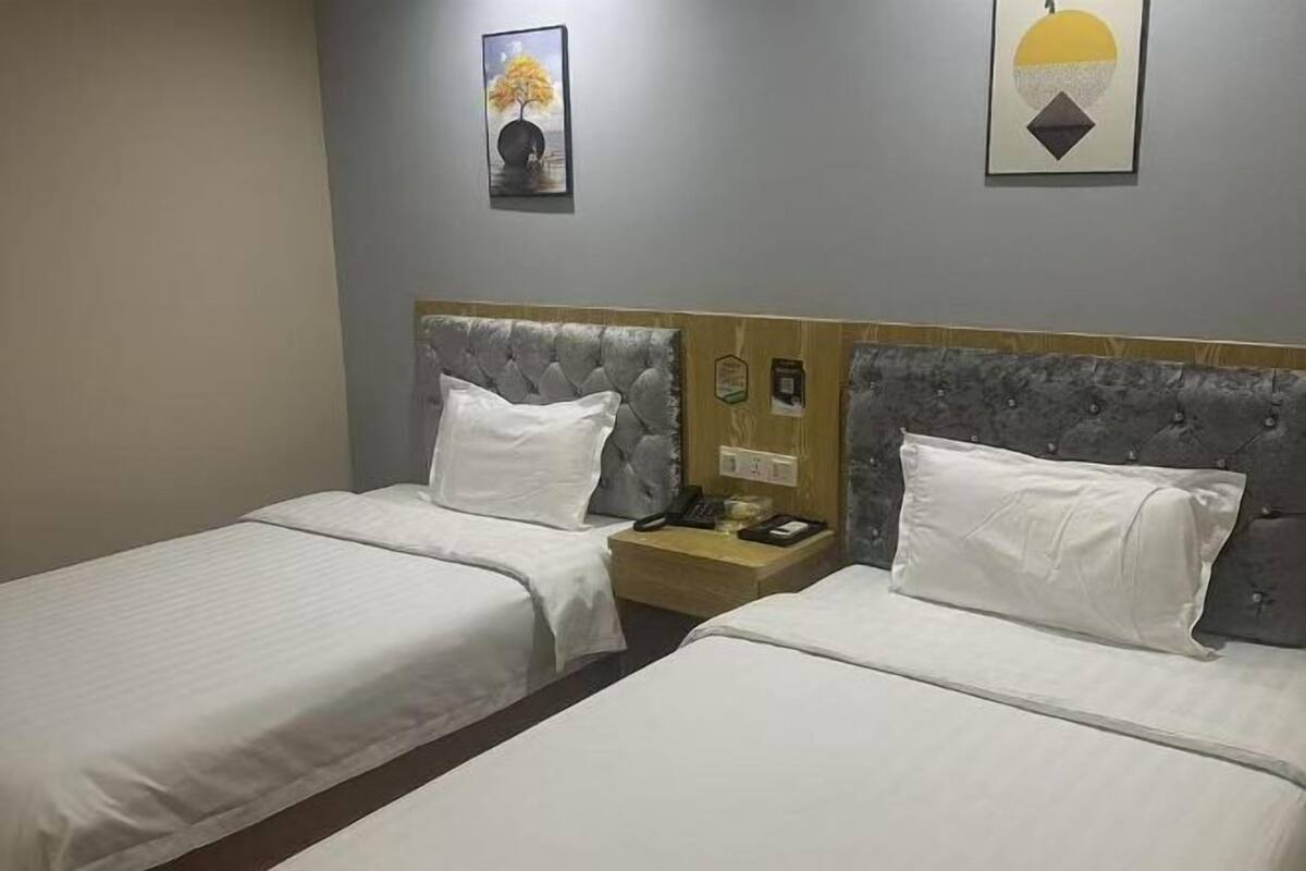 Habitación de hotel con dos camas, una mesita de noche de madera, un teléfono y dos cuadros en la pared.