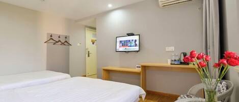 A hotel room with two beds, a television, a desk, and a chair with a vase of flowers.