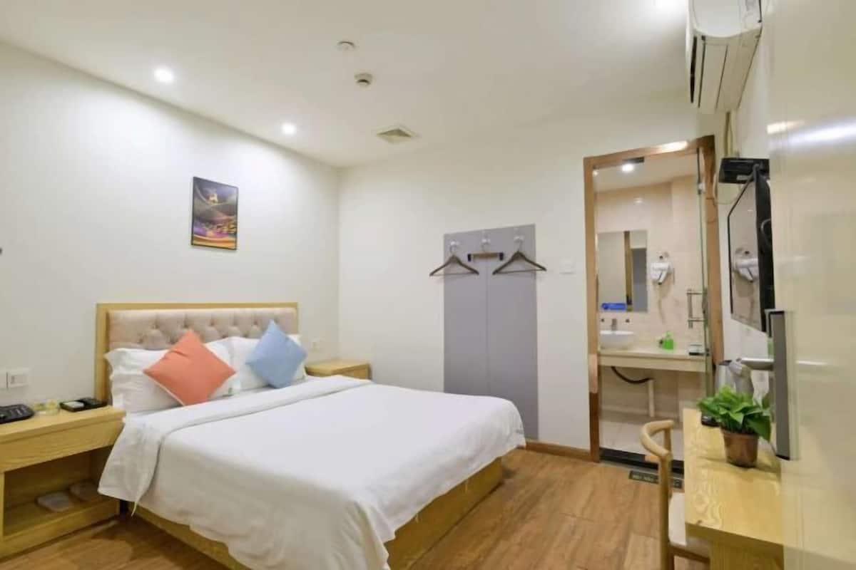Un dormitorio con cama, mesita de noche, armario y baño completo con lavamanos y espejo.