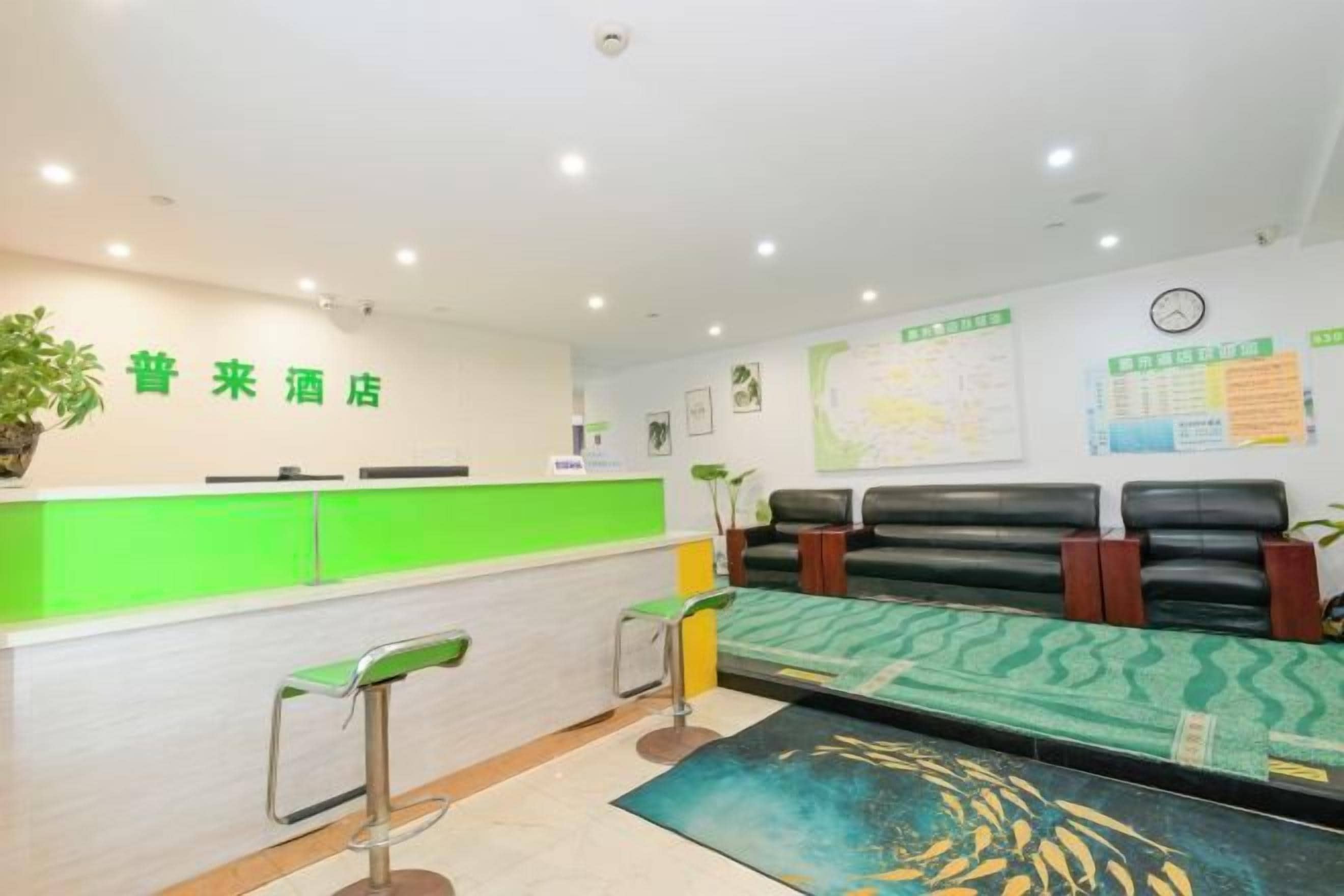 A hotel reception area with a green counter, a reception desk, and a seating area with a patterned rug.