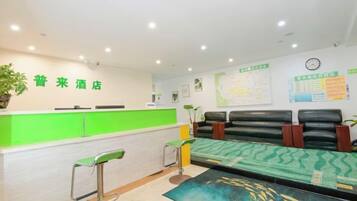Zona de recepción de un hotel con un mostrador verde, una mesa de recepción y un área de descanso con un tapete estampado.