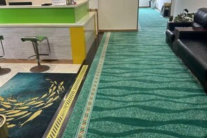 A reception area with a green counter, a patterned carpet, and a sofa. - Pulai Hotel (Zhoushan)