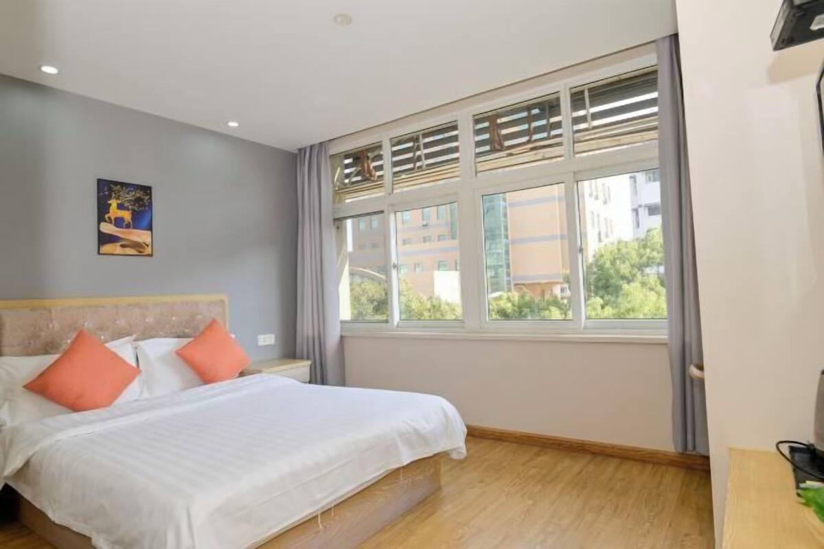 Un dormitorio con cama, ventana con persianas, un cuadro en la pared y suelo de madera.