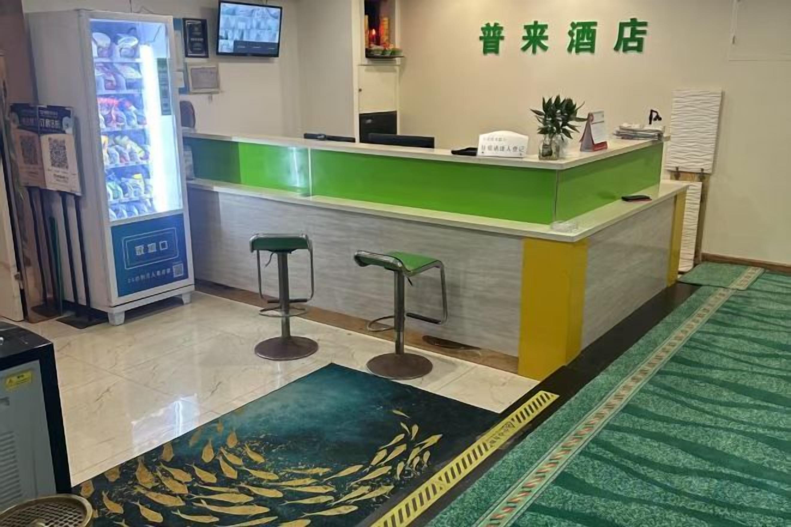 A hotel reception area with a green counter, two bar stools, a vending machine, and a patterned carpet.