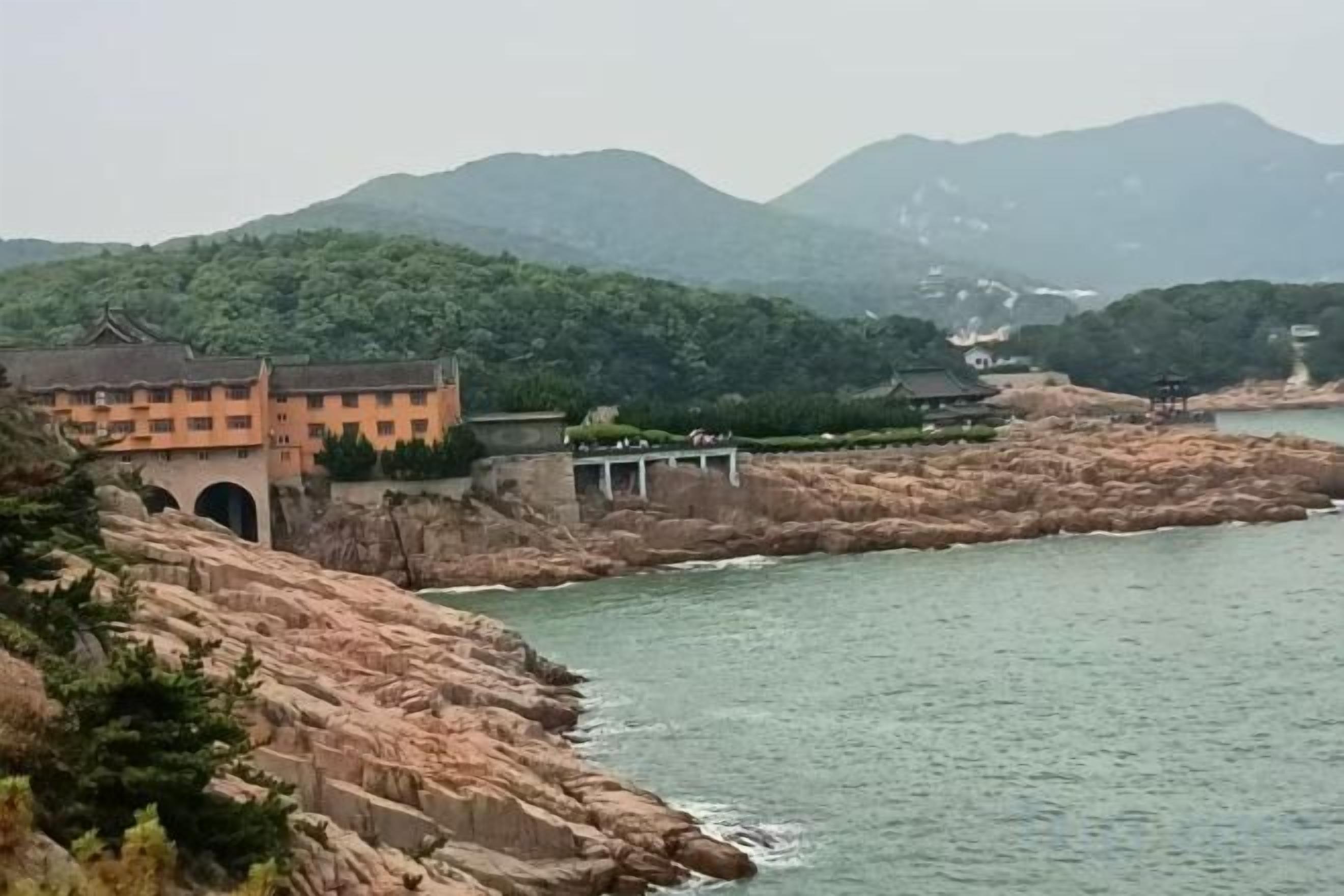 Un edificio de estilo arquitectónico tradicional, situado cerca de una masa de agua con un puente que lo conecta a una extensión de tierra más grande.