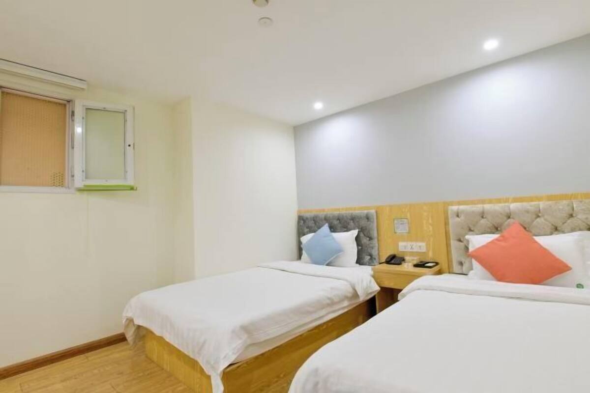 Una habitación de hotel con dos camas individuales, una mesita de noche con teléfono y una ventana con persianas.