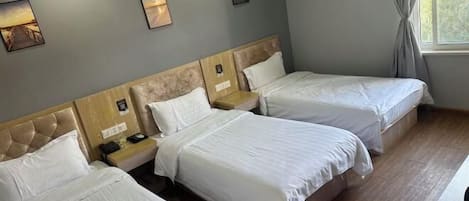 A hotel room with three single beds, a wooden headboard, a bedside table with a lamp, and a window with curtains.