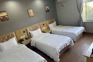 Habitación de hotel con tres camas individuales, cabecera de madera, mesita de noche con lámpara y ventana con cortinas.