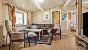 Ein gemütliches Zimmer mit einer braunen Ledersofa, zwei Sesseln, einem kleinen Tisch und einem Fernseher auf einem Holzregal.