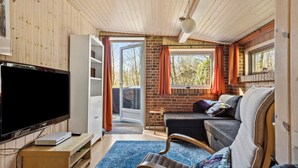 Ein gemütliches Zimmer mit Fernseher, einem kleinen Tisch, einer Couch und einem Fenster mit Vorhängen.