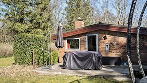 Ein Ziegelhaus mit einer überdachten Terrasse, einem Metallschirm und einem kleinen Garten.