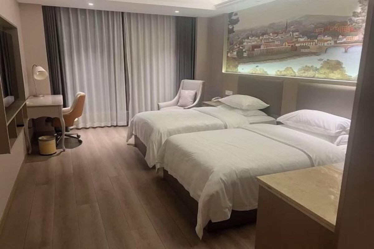 Une chambre d’hôtel avec deux lits, un bureau, une chaise et une grande fenêtre donnant sur un beau paysage.