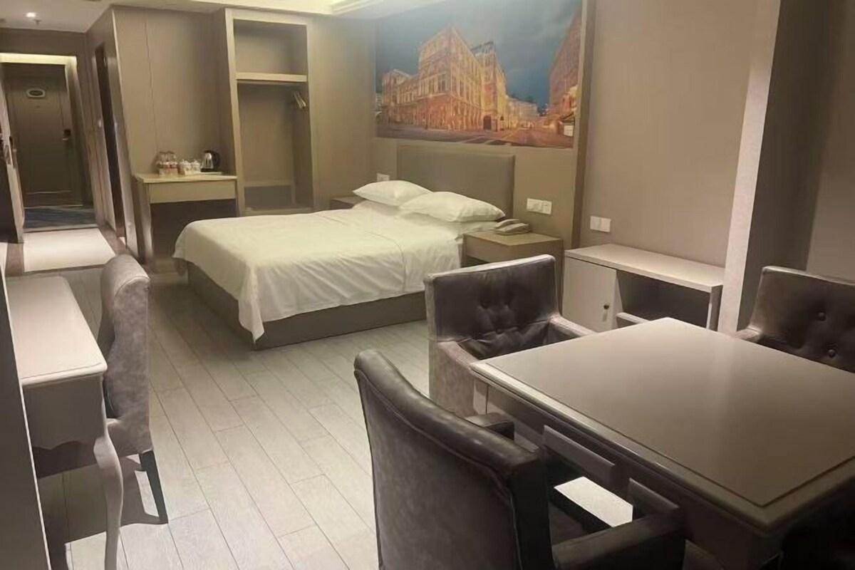 A compact hotel room with a bed, a desk, a chair, and a small table.