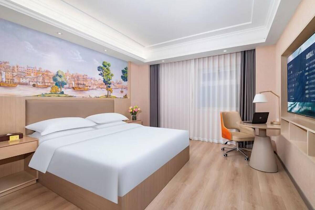 A hotel room with a large bed, a desk with a chair, a TV, and a mural on the wall.