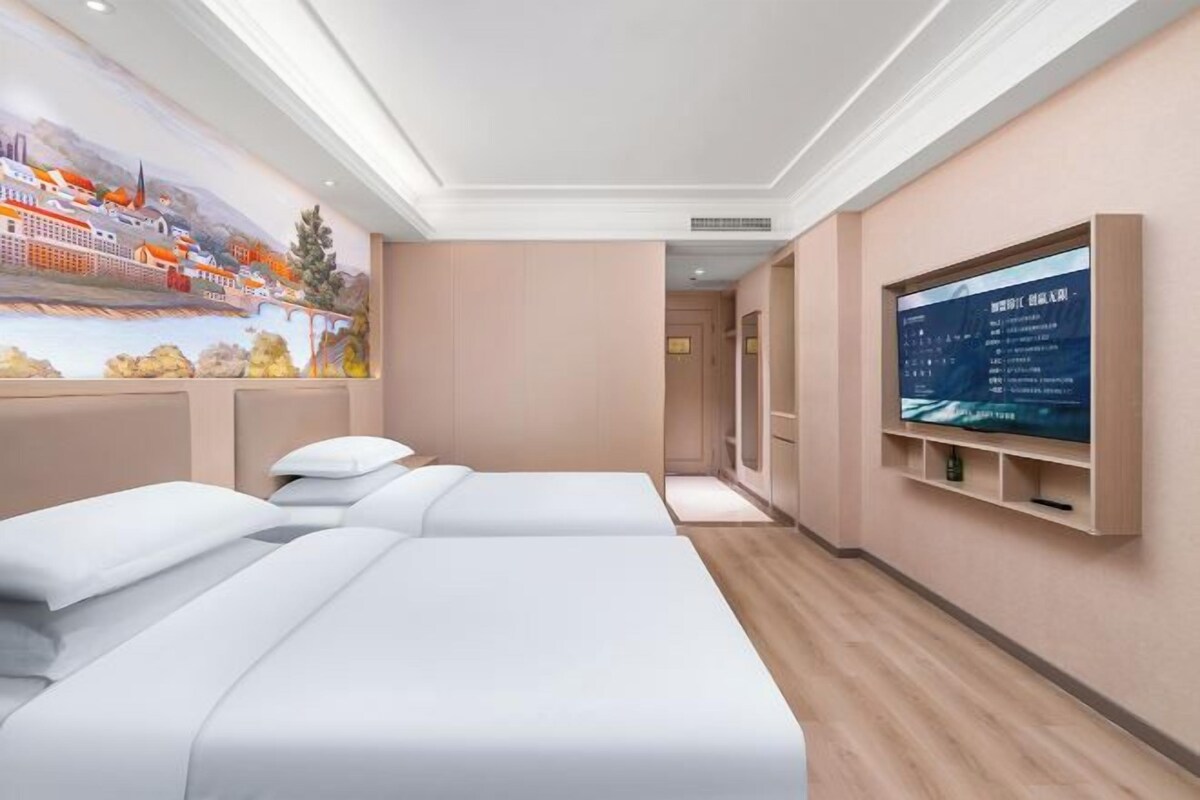 A hotel room with two beds, a mural on the wall, a TV, and a wooden floor.