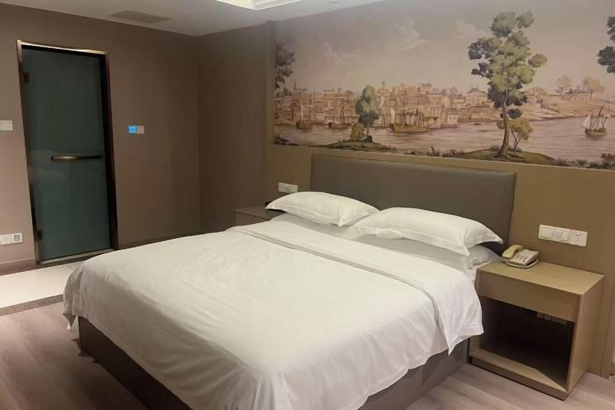 A hotel room with a bed, a nightstand with a phone, a door, and a mural on the wall.