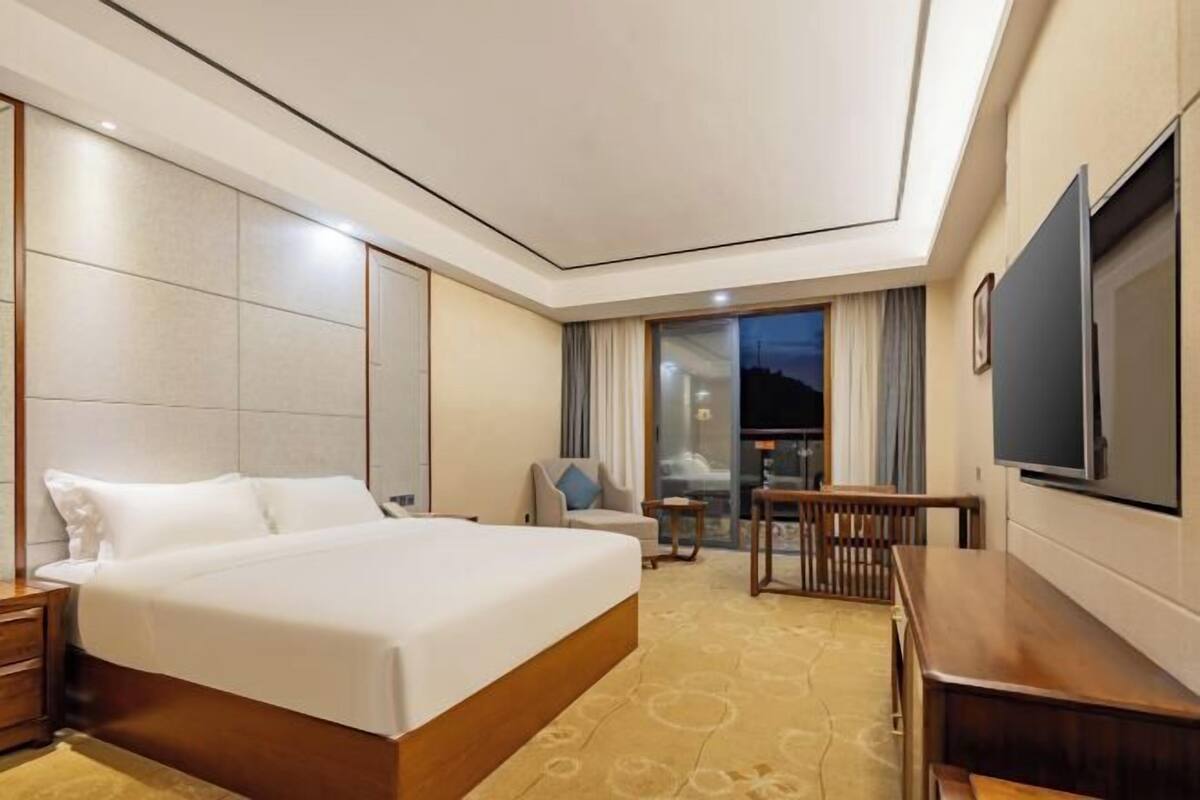 Habitación de hotel con una cama grande, un escritorio, una silla, un televisor y vistas al exterior.