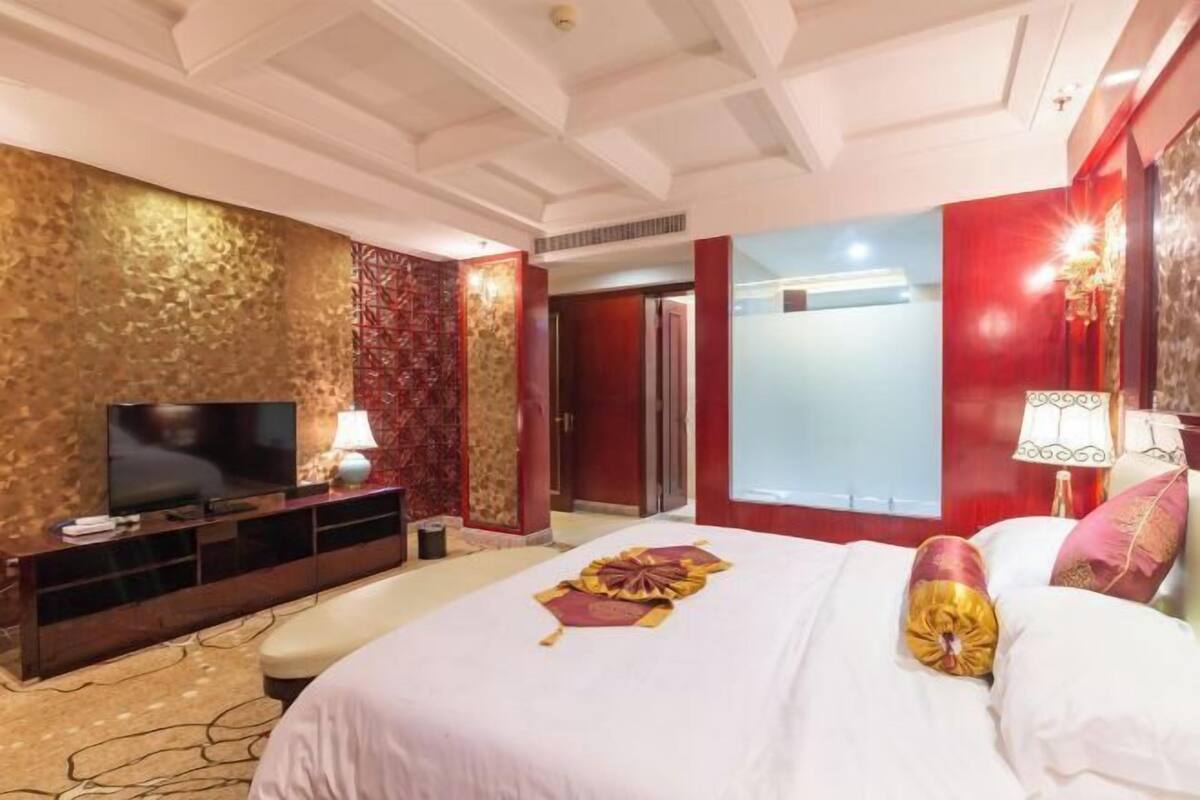 Habitación de hotel con una cama grande, un televisor de pantalla plana, un escritorio con lámpara y una pared de acento roja.