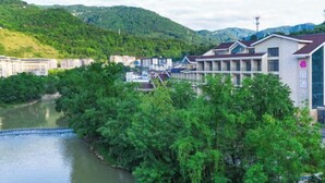 A riverside hotel with multiple buildings, a river, and lush greenery in the background. - Wufeng International Hotel (Wufeng)