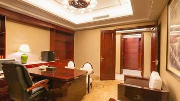 A hotel room with a desk, chairs, a telephone, a lamp, and a large mirror.