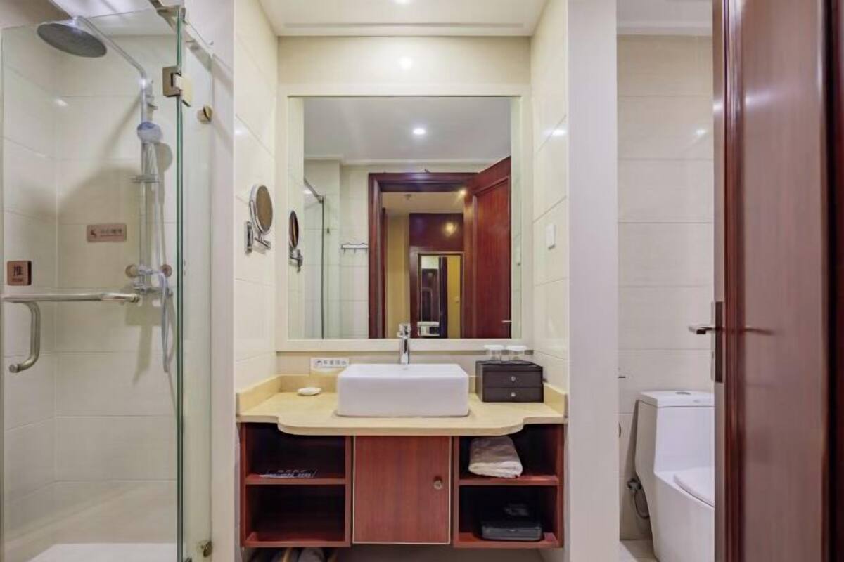 Un baño con ducha de vidrio, lavamanos blanco, espejo y tocador de madera.