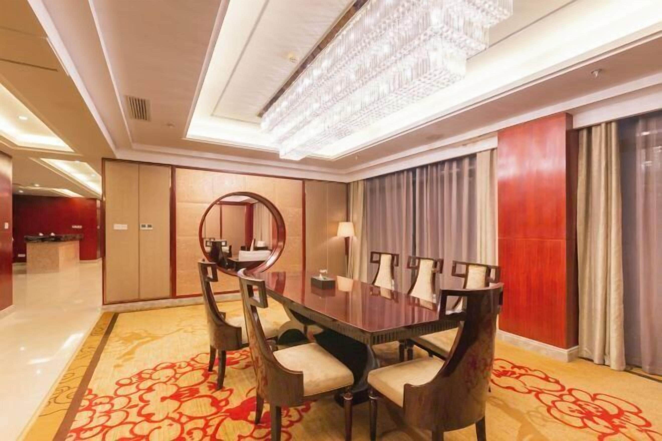 Una sala conferenze con un grande tavolo rettangolare, diverse sedie, un lampadario e un tappeto a motivi.