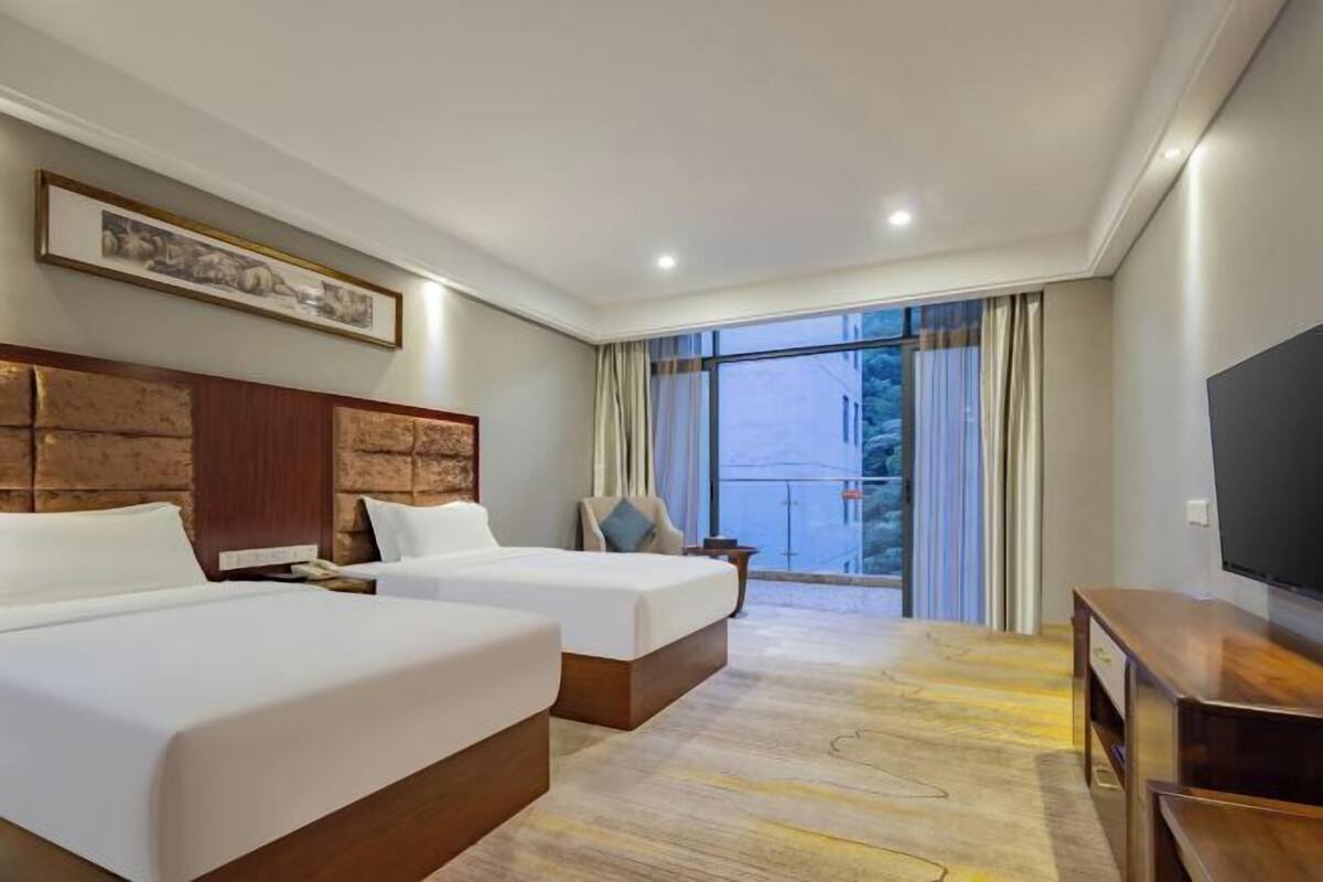 Habitación de hotel con dos camas, televisión y un ventanal grande con cortinas.