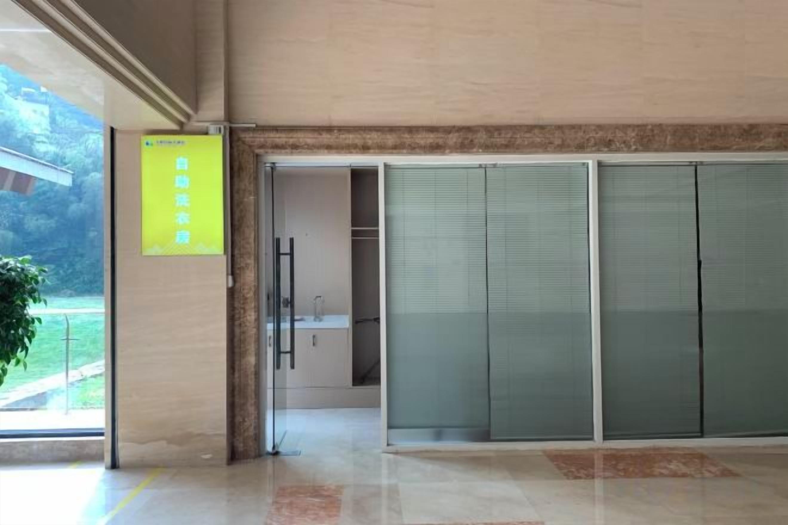 A hotel lobby with a sliding glass door entrance, a reception desk, and a yellow sign on the wall.