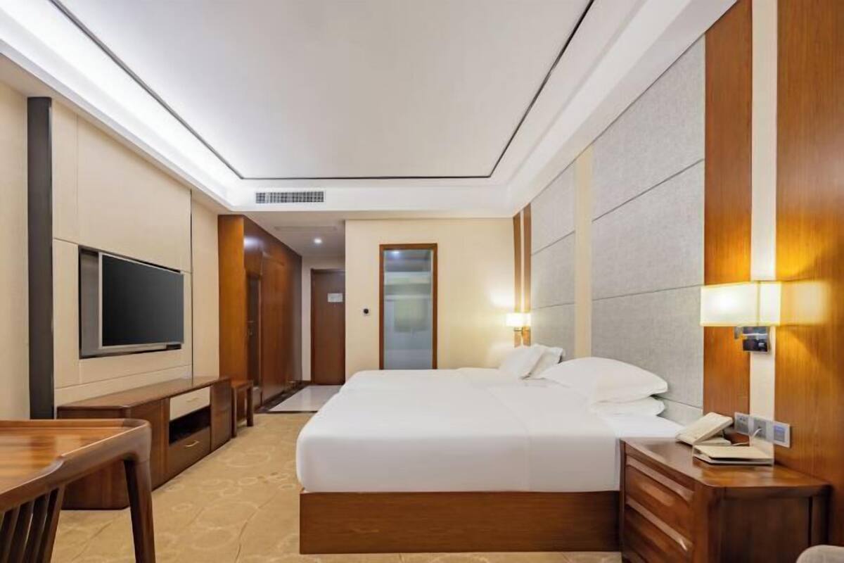 Una habitación de hotel con una cama grande, televisión, escritorio y mesita de noche con lámpara.