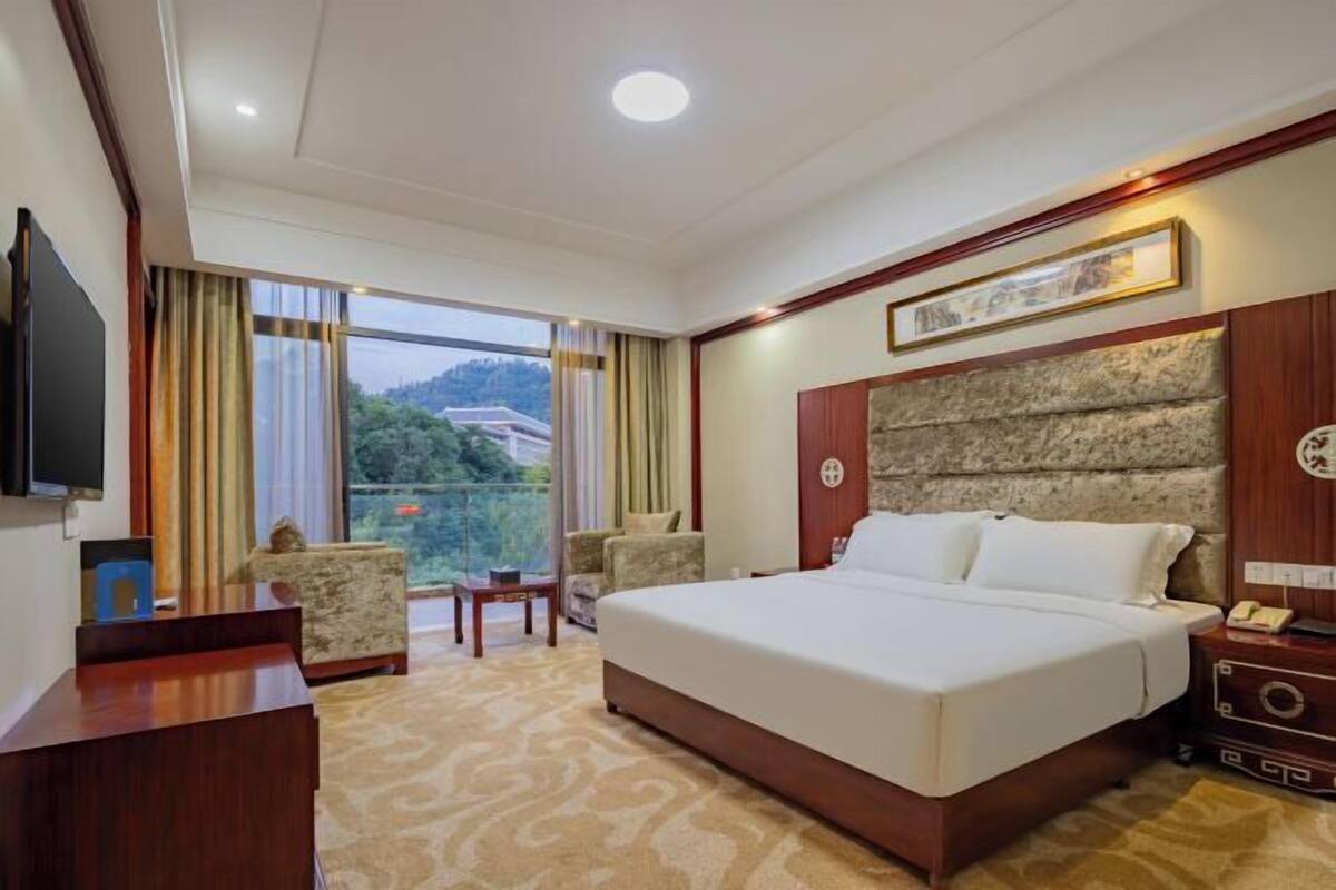 Habitación de hotel con una cama grande, televisión, escritorio y vistas a zonas verdes.