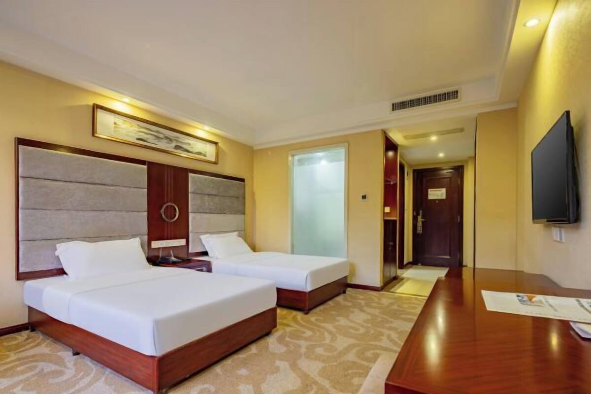 Habitación de hotel con dos camas, un escritorio, un televisor y un cuadro en la pared.